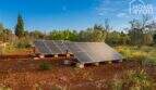 Ground-level solar system on red earth of the finca near Felanitx, surrounded by Mediterranean vegetation.