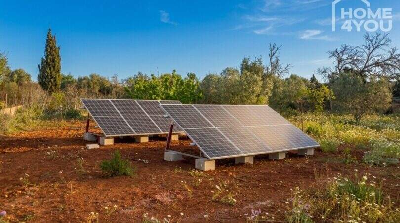 Ground-level solar system on red earth of the finca near Felanitx, surrounded by Mediterranean vegetation.