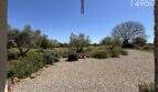 Gravelly outdoor area of Finca Felanitx with fireplace, olive trees and Mediterranean planting under blue sky.