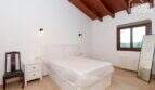 Helles Schlafzimmer der Finca mit Holzbalkendecke, Doppelbett, Parkettboden und Fenster mit Ausblick.
