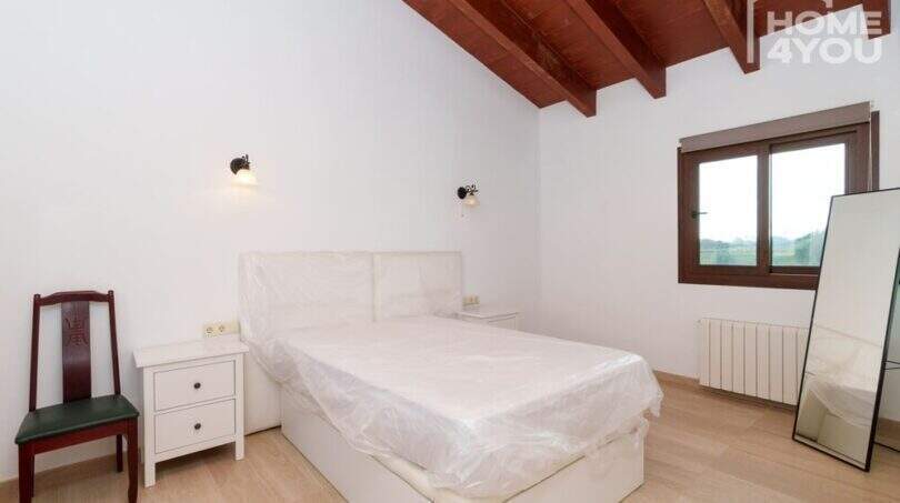 Helles Schlafzimmer der Finca mit Holzbalkendecke, Doppelbett, Parkettboden und Fenster mit Ausblick.