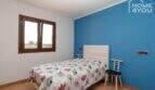 Schlafzimmer mit blauer Akzentwand, Einzelbett, Holzboden und Fenster mit Landschaftsblick in moderner Finca