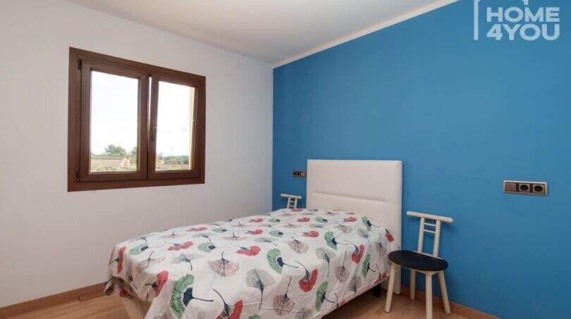 Schlafzimmer mit blauer Akzentwand, Einzelbett, Holzboden und Fenster mit Landschaftsblick in moderner Finca
