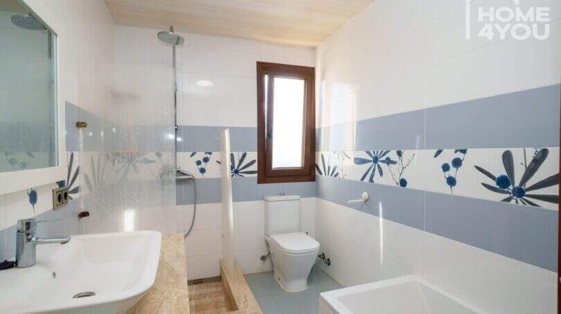 Helles Badezimmer der Finca mit Dusche, Badewanne, WC und blau-weißen Blumenfliesen.