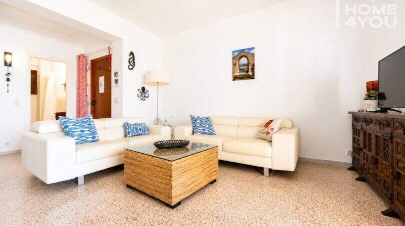 Luminosa sala de estar con sofás de cuero blanco, mesa de cristal y decoración mediterránea en Ses Salines, apartamento de 125 m².