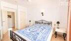 Luminoso dormitorio con cama doble, marco de metal negro, ropa de cama azul y blanca y ventilador de techo