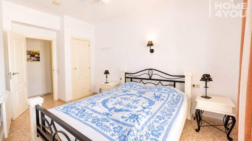 Luminoso dormitorio con cama doble, marco de metal negro, ropa de cama azul y blanca y ventilador de techo