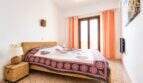 Luminoso dormitorio con cama doble, muebles de ratán y cortinas naranjas en apartamento con vista al mar, Ses Salines.