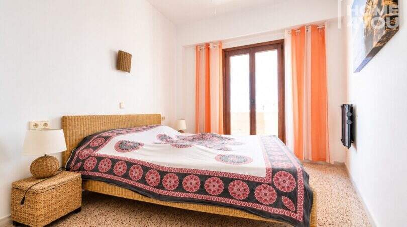 Luminoso dormitorio con cama doble, muebles de ratán y cortinas naranjas en apartamento con vista al mar, Ses Salines.