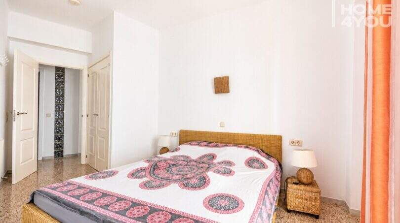 Luminoso dormitorio con cama doble, muebles de ratán y colcha multicolor en apartamento con vista al mar en Ses Salines.