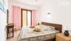 Luminoso dormitorio con cama doble, cabecero de ratán, cortinas rosas, acceso al balcón y ventilador de techo en Ses Salines