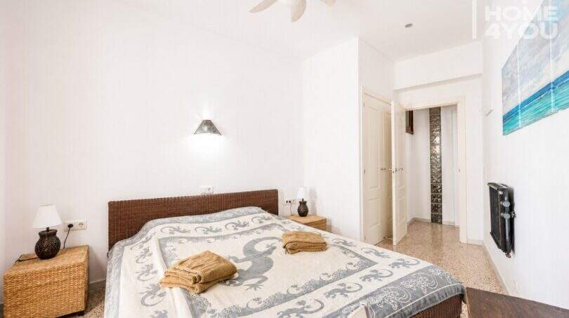 Luminoso dormitorio con cama doble, muebles de ratán, ventilador de techo y obra de arte con vista al mar en apartamento Ses Salines.