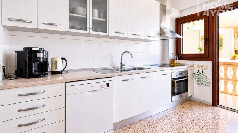 Moderna cocina blanca con lavavajillas, horno, cafetera y acceso a la terraza, apartamento Ses Salines