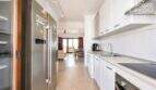 Cocina moderna con refrigerador de acero inoxidable y armarios empotrados blancos, vista a la luminosa sala de estar con acceso a la terraza
