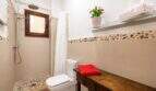 Luminoso baño con ducha, suelo de guijarros, estantería de madera y planta decorativa en apartamento en Ses Salines.
