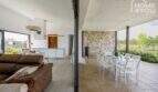 Zona de cocina-estar abierta con terraza, muebles de exterior blancos y pared de piedra natural mediterránea de la finca en Sa Pobla