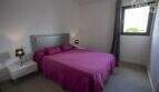 Dormitorio de la finca en Sa Pobla con cama doble, ropa de cama morada, cabecero plateado y ventana con cortinas.