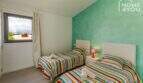 Dormitorio con 2 camas individuales, colchas de colores, pared de acento turquesa y vista a las montañas a través de la ventana
