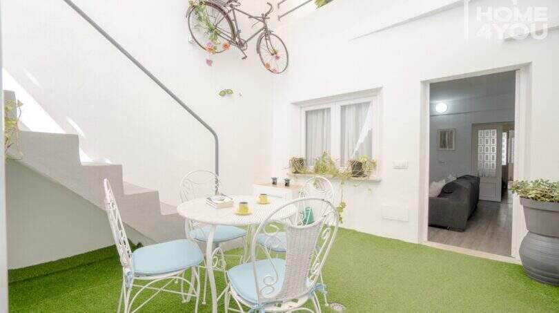 Innenpatio mit Kunstrasen, weißen Bistrostühlen und dekorativem Fahrrad an der Wand, Stadthaus Maria de la Salut