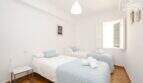 Helles Schlafzimmer mit drei Einzelbetten, hellblauen Decken, Fliesenboden und weißem Fenster im Stadthaus Maria de la Salut