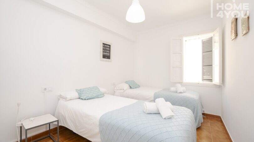 Helles Schlafzimmer mit drei Einzelbetten, hellblauen Decken, Fliesenboden und weißem Fenster im Stadthaus Maria de la Salut