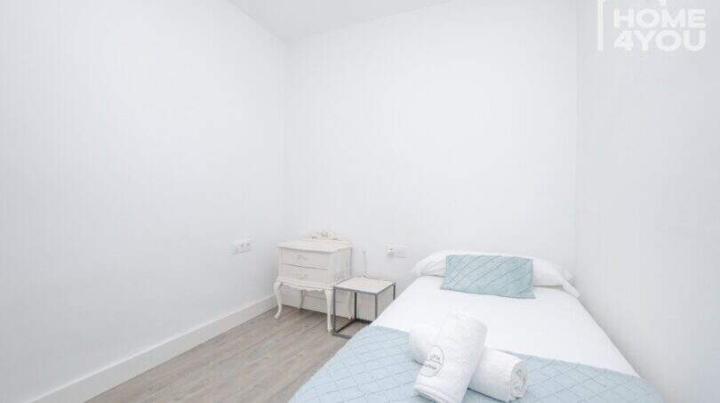 Helles Schlafzimmer mit Einzelbett, mintfarbener Bettwäsche, weißem Nachttisch und hellem Holzboden im Stadthaus Maria de la Salut