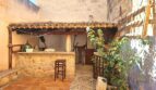 Rustikaler Patio mit Natursteinbar, Terrakottaboden, Holzdach und Bepflanzung – charmantes Stadthaus in Petra