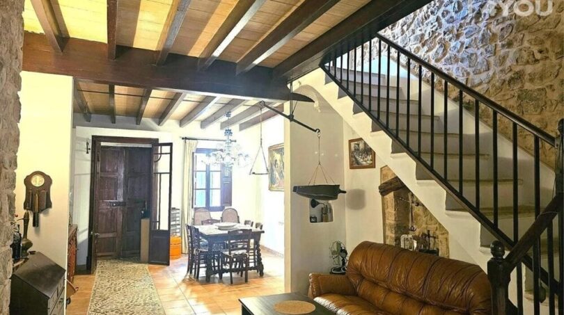 Rustikales Wohnzimmer mit Holzbalkendecke, Ledersofa, Natursteinwand und Treppe zum Obergeschoss