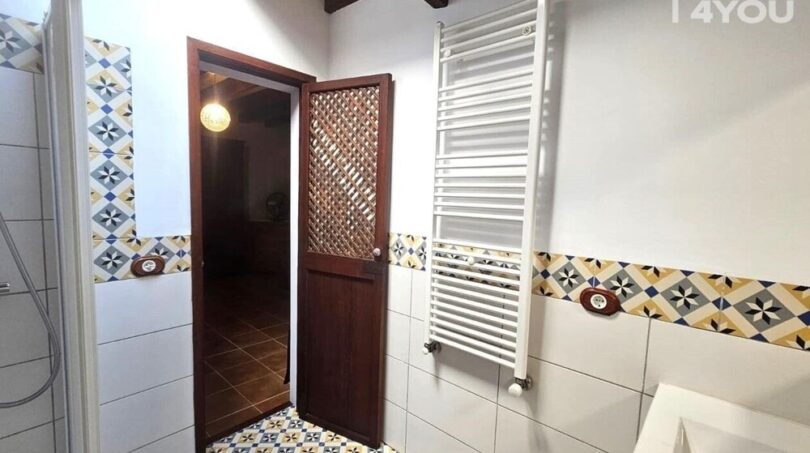 Badezimmer mit bunten Mosaikfliesen, Handtuchheizkörper, Holzbalken und rustikaler Holztür im Stadthaus Petra