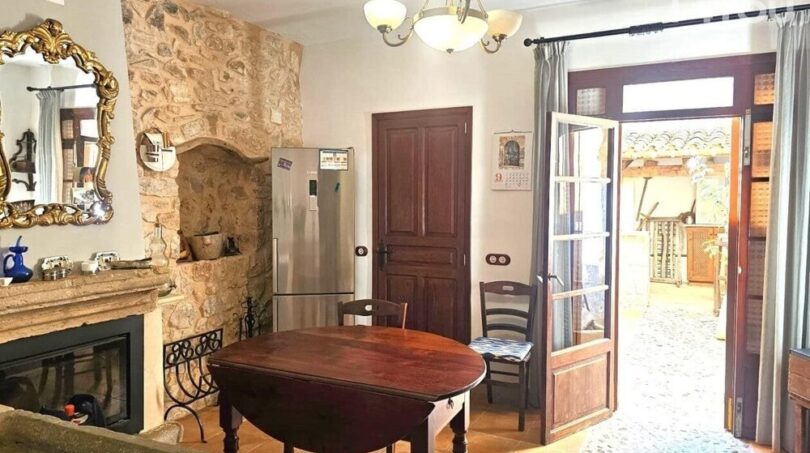 Wohnzimmer mit Natursteinwand, Kamin, antikem Holztisch und französischer Tür zum Patio