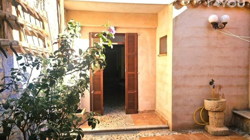 Mediterraner Innenpatio mit Holzlamellentür, Natursteinbrunnen, Bougainvillea und Terrakottafliesen eines Stadthauses in Petra