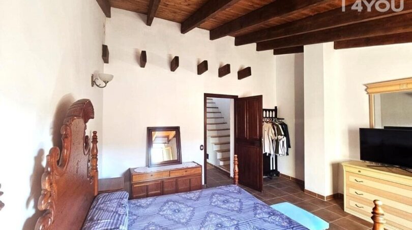 Schlafzimmer mit Holzbalkendecke, antikem Bett, Kleiderstange und TV im Stadthaus Petra