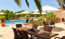 Sonnige Poolterrasse mit Rattanmöbeln, Sonnenschirmen und Steinmauer des Agroturismo bei Ses Salines