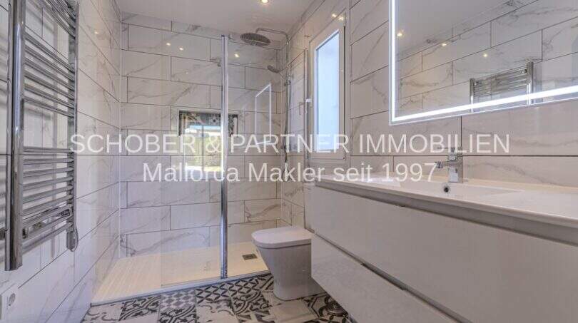 Modernes Badezimmer mit Marmorfliesen, begehbarer Dusche, WC und beleuchtetem Spiegel in mediterraner Villa Sa Coma