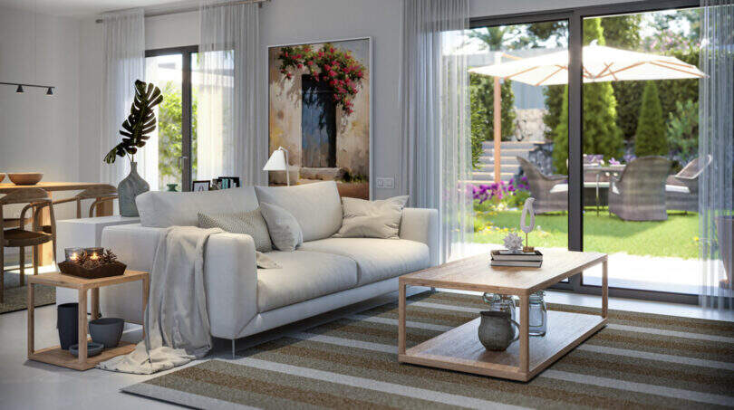 Helles Wohnzimmer mit weißem Sofa, Holztisch und großer Glasfront zum gepflegten Garten, Reihenhaus Esporles