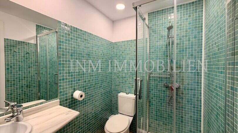 Badezimmer der Dachgeschosswohnung Blanquerna Palma mit grünen Mosaikfliesen, Glasdusche und Marmorwaschbecken