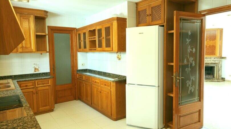 Geräumige Küche mit Holzschränken, Granit-Arbeitsplatten und Kühlschrank in der Hafenwohnung Porto Cristo