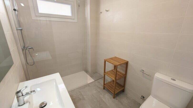 Modernes Badezimmer der Hafenwohnung Porto Cristo mit Dusche, WC, Waschbecken und Holzregal