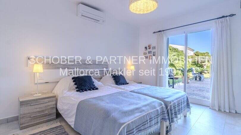 Helles Schlafzimmer mit Doppelbett, blauer Dekoration, Klimaanlage und Zugang zur sonnigen Terrasse der mediterranen Villa.