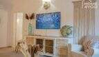 Helles Wohnzimmer mit TV, Holzkommode, Sessel & Boho-Deko im Bungalow in Alcúdia, Mallorca.