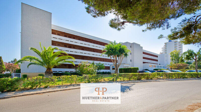 Außenansicht Apartment-Komplex in Cales de Mallorca mit Palmen, gepflegter Grünanlage und rotem Klinkerfassade.