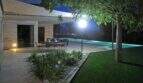 Beleuchtete Terrasse mit Esstisch, Infinity-Pool und Gartenanlage der modernen Finca in Felanitx bei Nacht.