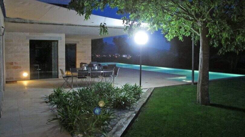 Beleuchtete Terrasse mit Esstisch, Infinity-Pool und Gartenanlage der modernen Finca in Felanitx bei Nacht.