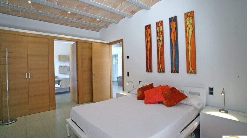Helles Schlafzimmer der Finca Felanitx mit Doppelbett, Gewölbedecke, Holzschiebetüren und farbenfrohen Wandgemälden.
