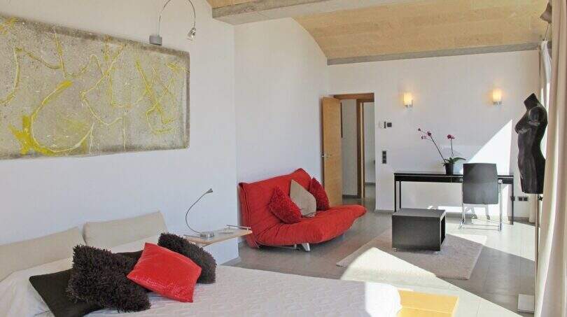 Helles Schlafzimmer der Finca Felanitx mit rotem Sessel, Kunstwerk, Natursteindecke und modernem Schreibtisch