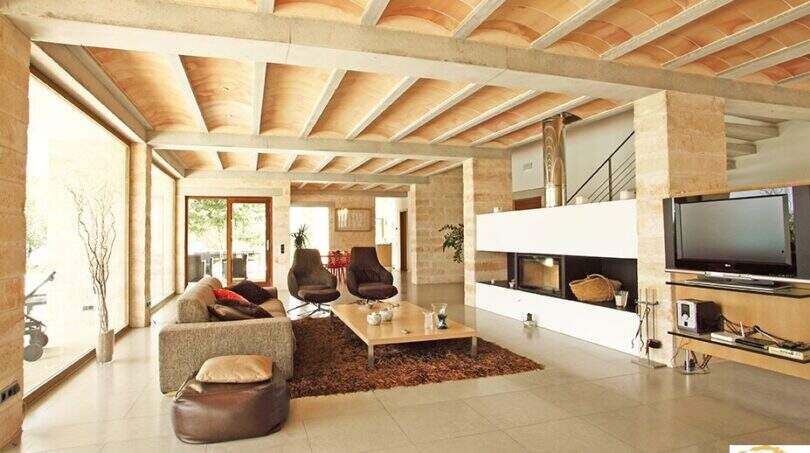 Geräumiges Wohnzimmer der Finca Felanitx mit Kamin, Natursteinwänden, gewölbter Holzdecke und modernem TV-Bereich.