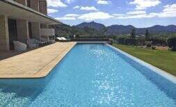 Gran piscina infinita con terraza de arenisca, área lounge y panorama montañoso de la finca moderna en Felanitx
