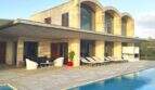 Moderne Finca in Felanitx: Poolbereich mit Sandsteinvilla, Arkadenfenstern und Liegestühlen auf der Terrasse.