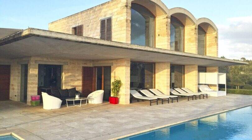 Moderne Finca in Felanitx: Poolbereich mit Sandsteinvilla, Arkadenfenstern und Liegestühlen auf der Terrasse.