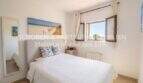 Bright bedroom with white double bed, ocean view picture and window with view in Son Servera